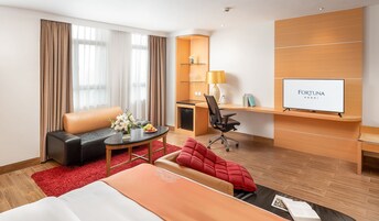 A hotel room with a bed, a desk, a chair, a TV, and a red carpet.