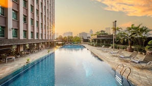 Una piscina con sillas de descanso y un paisaje urbano al fondo.