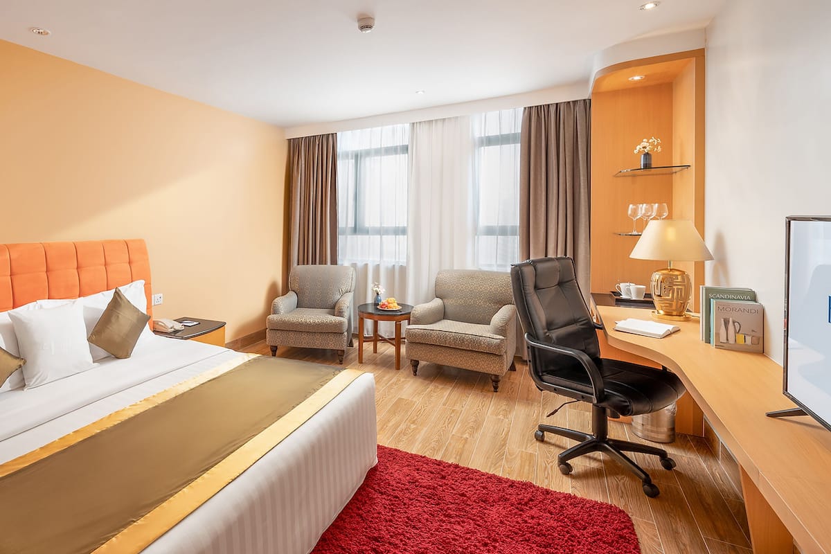A hotel room with a bed, two armchairs, a desk, and a TV.