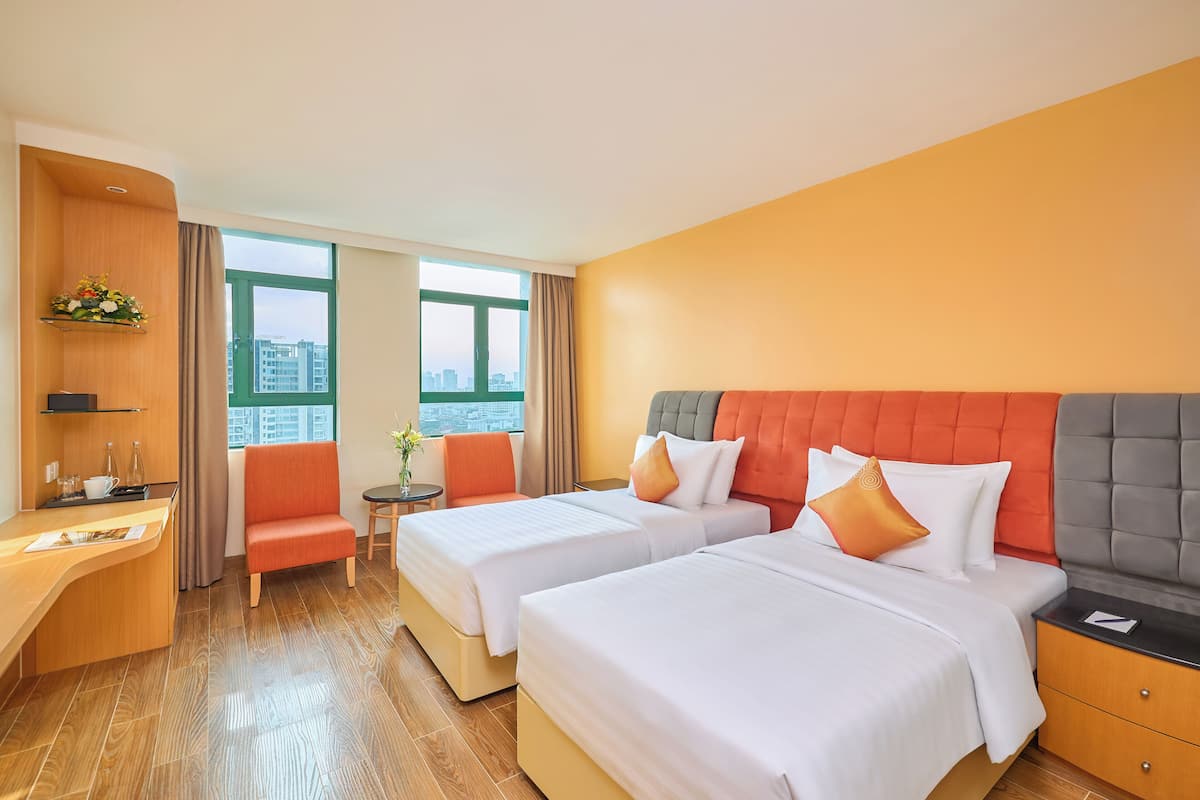 A hotel room with two beds, a desk, a chair, and a view of the city.
