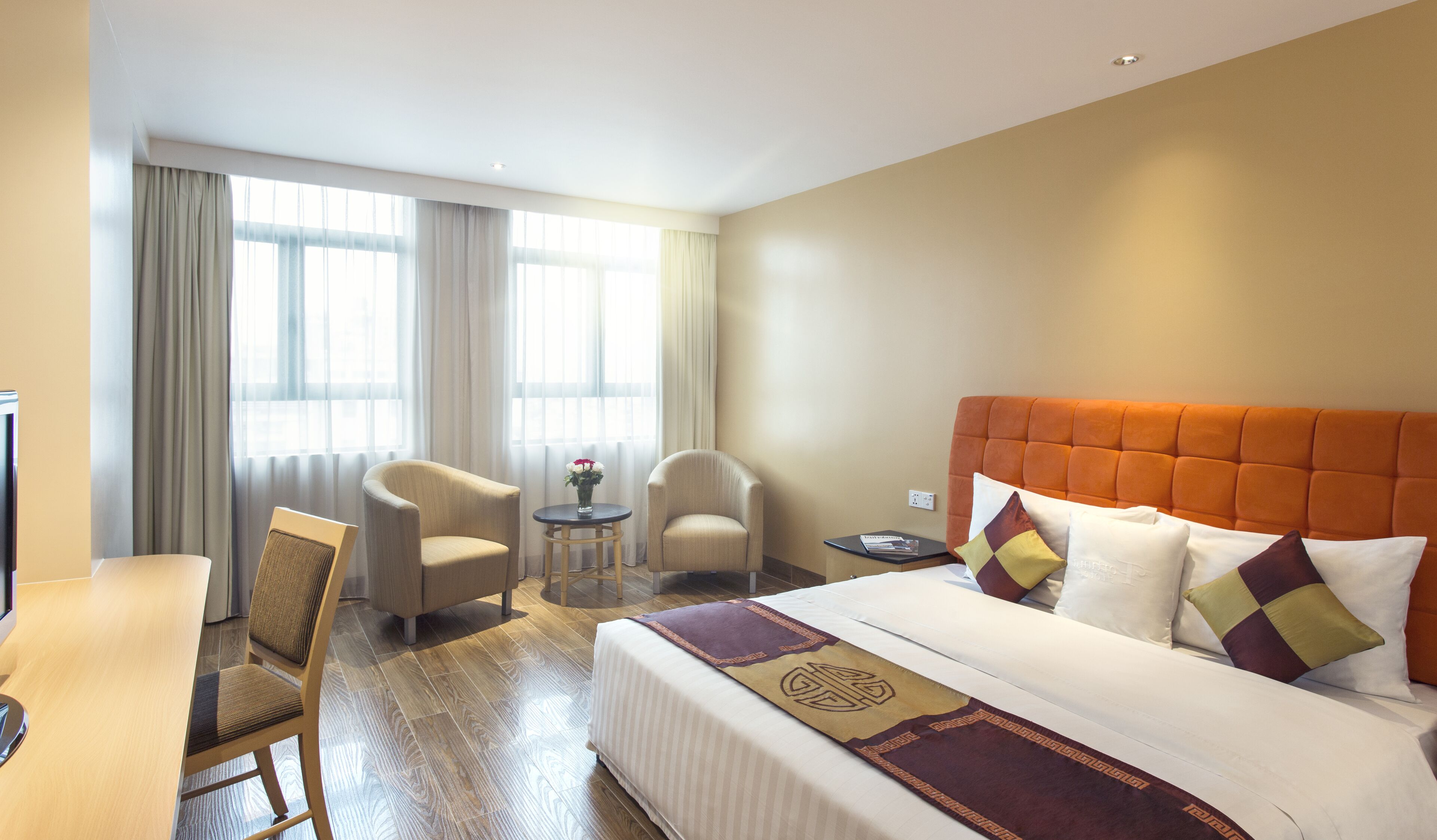 A hotel room with a bed, two armchairs, a small table, and a TV.