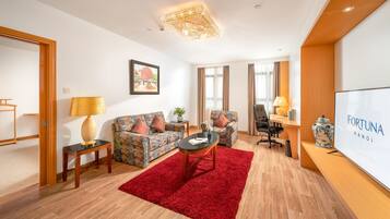 A modern hotel room with a sofa, armchair, desk, and a red rug.