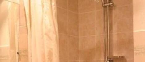 A shower with a handheld showerhead, a curtain, and a tiled wall.