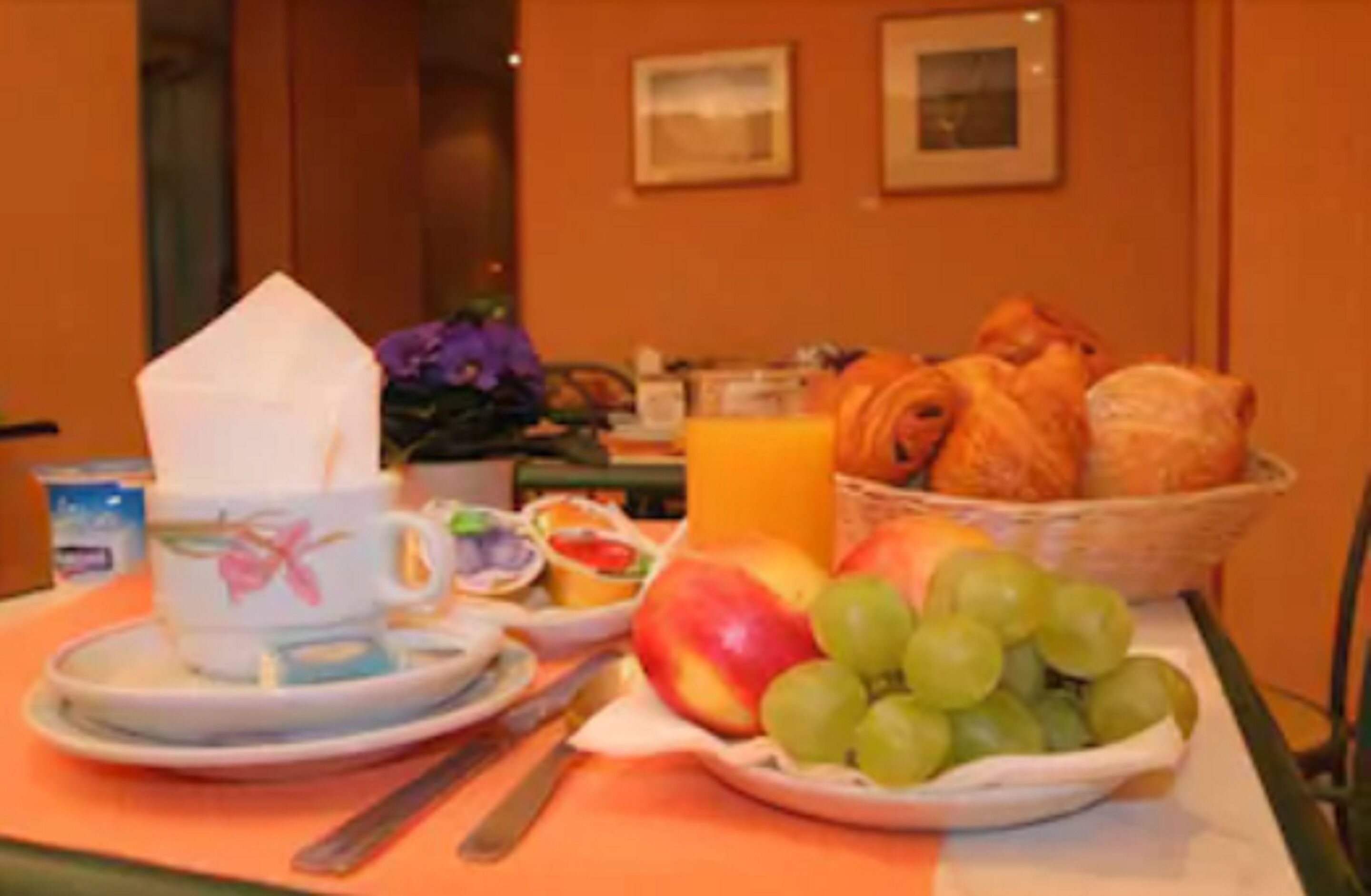 A breakfast table with a cup, saucer, knife, fruit, and pastries.