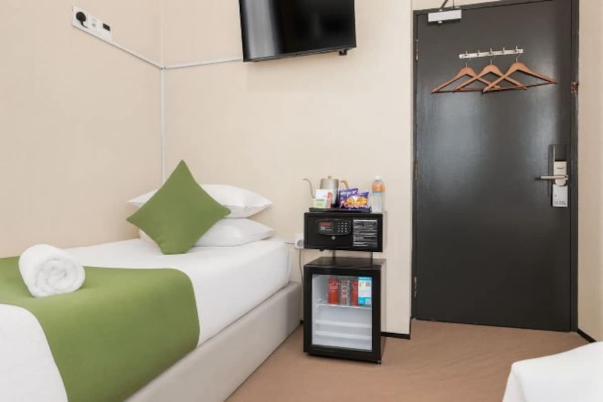 A hotel room with a bed, a small refrigerator, a television mounted on the wall, and a door with a coat rack.