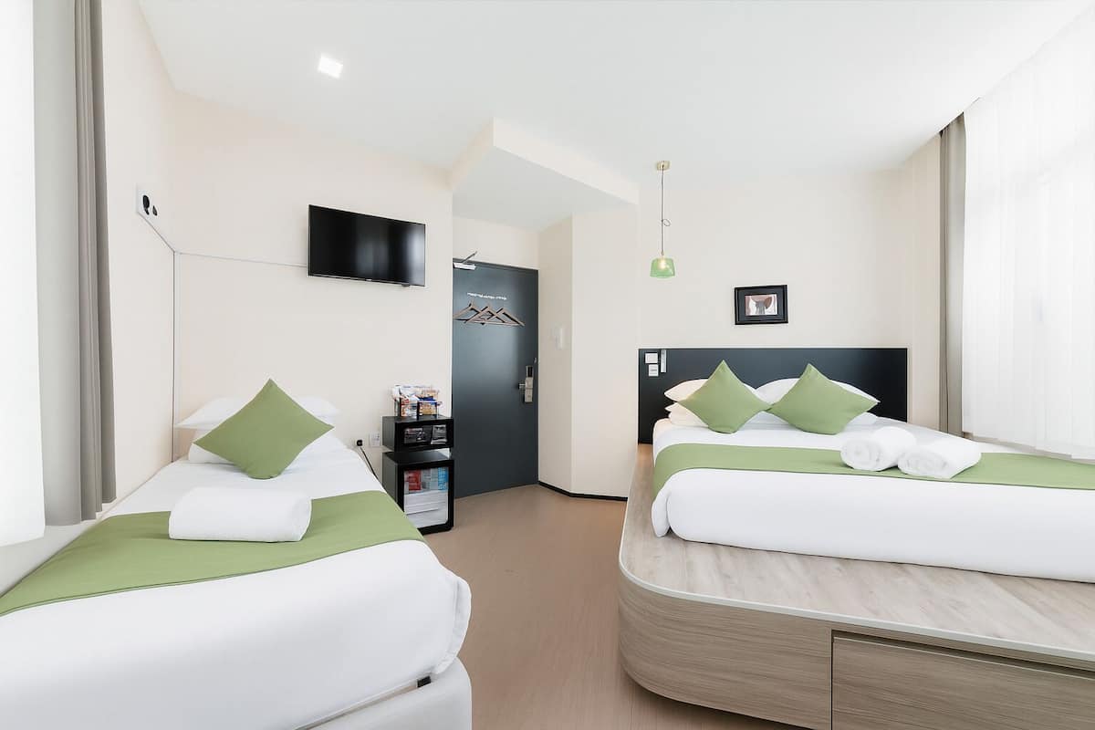 Quarto de hotel com duas camas, televisão, minibar e porta que dá para outro quarto.