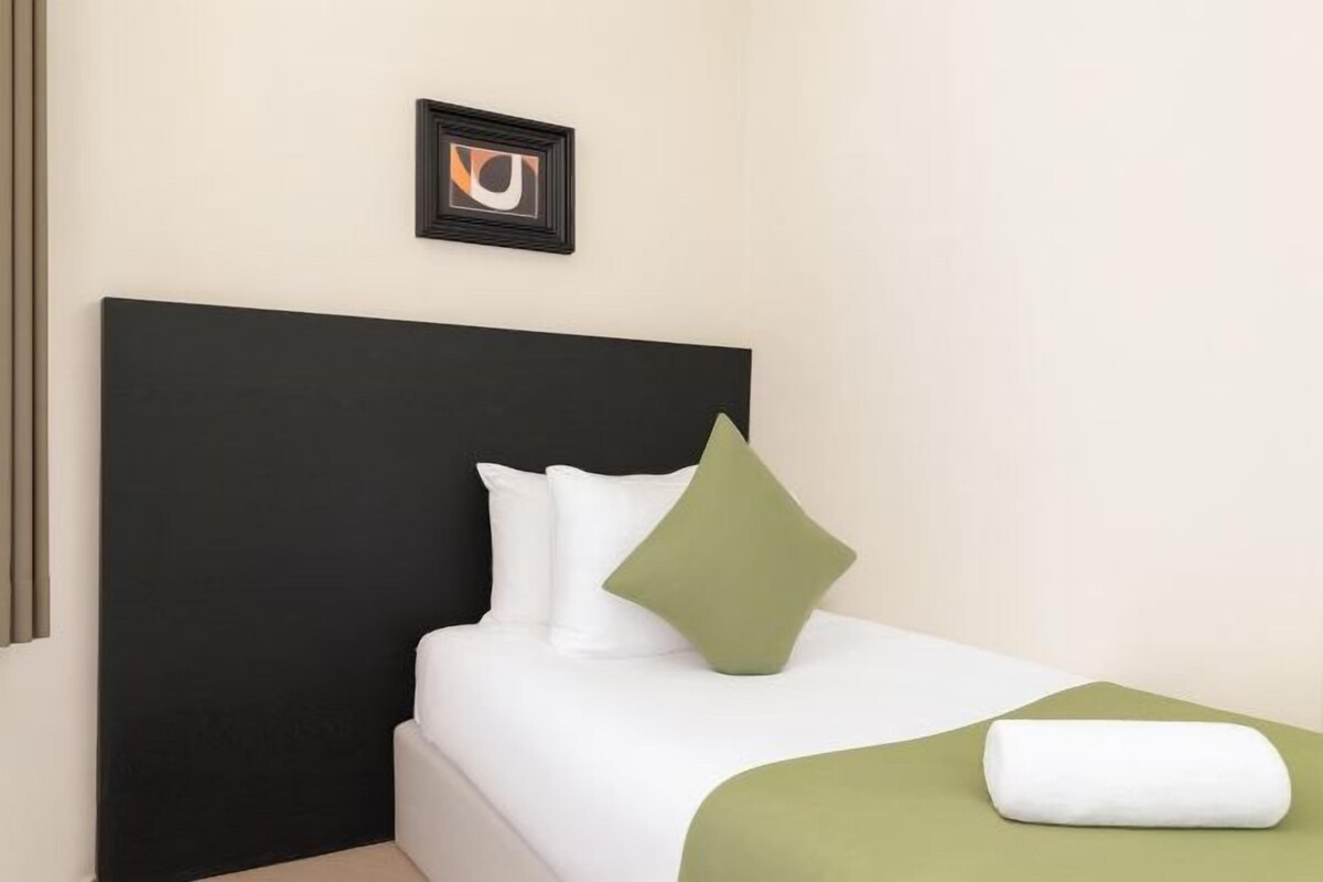 A hotel room with a black headboard, white bedding, a green pillow, and a framed picture on the wall.