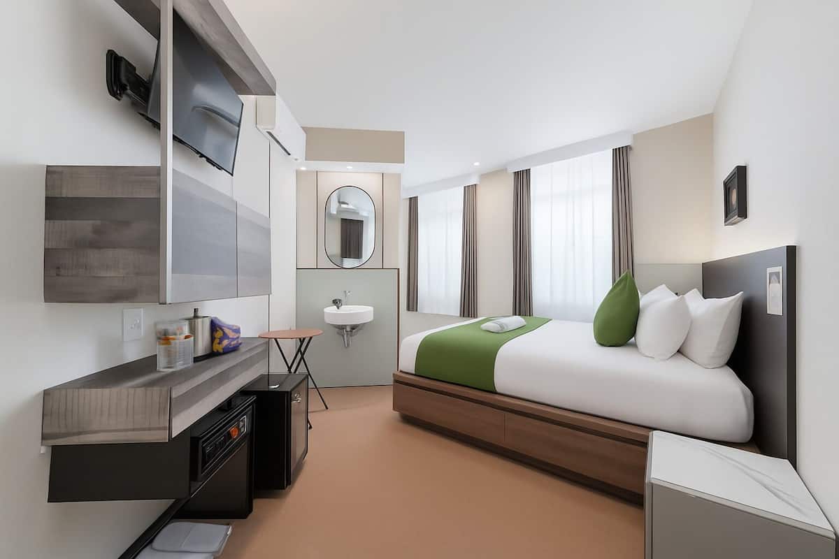 Quarto de hotel moderno com cama, mesa de cabeceira, escrivaninha e um espelho grande.