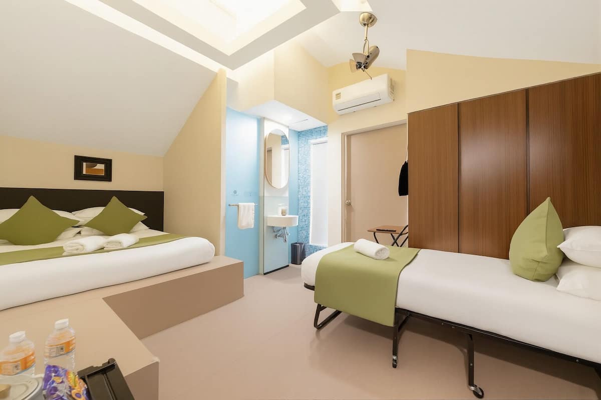 Quarto de hotel com duas camas, banheiro e claraboia.