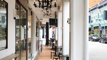 Un área de café al aire libre con mesas y sillas, un candelabro moderno y vista a la calle.