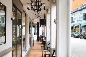 An outdoor cafe area with tables and chairs, a modern chandelier, and a view of the street. - A Hotel Chinatown (Singapore)