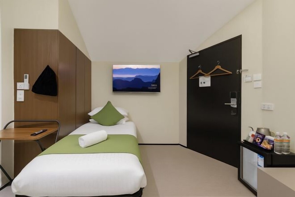A hotel room with a bed, a TV mounted on the wall, a desk with a chair, and a door with a coat hanger.