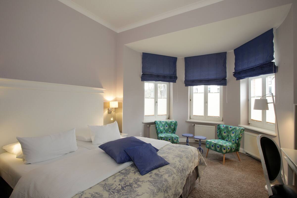 A hotel room with a bed, two chairs, a desk, and a radiator.