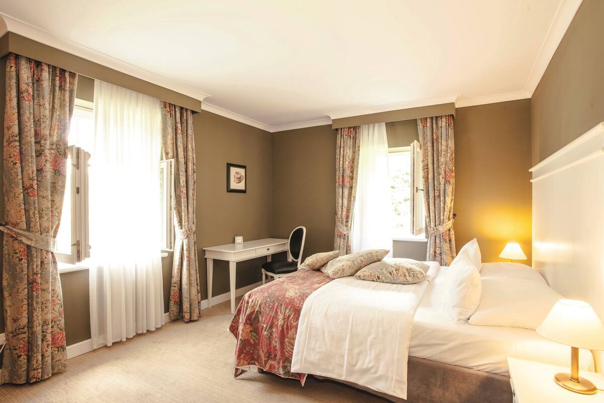 A hotel room with a bed, desk, chair, and a lamp.