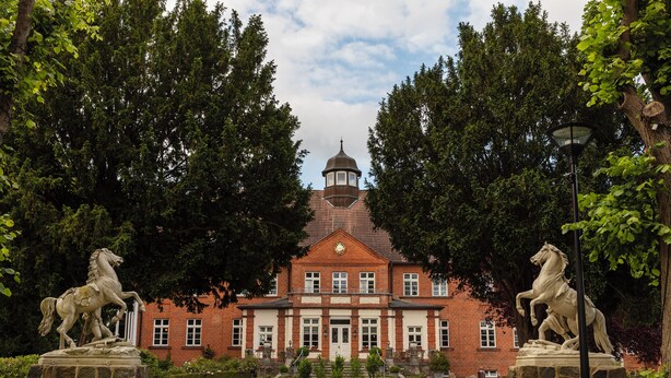A brick building with a central dome and two horse statues in front.