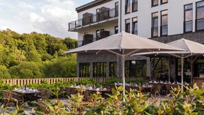An outdoor dining area with tables and chairs, umbrellas, and a building with balconies in the background.