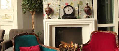 A room with a fireplace, two armchairs, a table, and a deer head mounted on the wall.