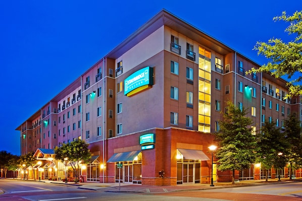 A multi-story hotel with a prominent Staybridge sign, a covered entrance, and a well-lit facade.