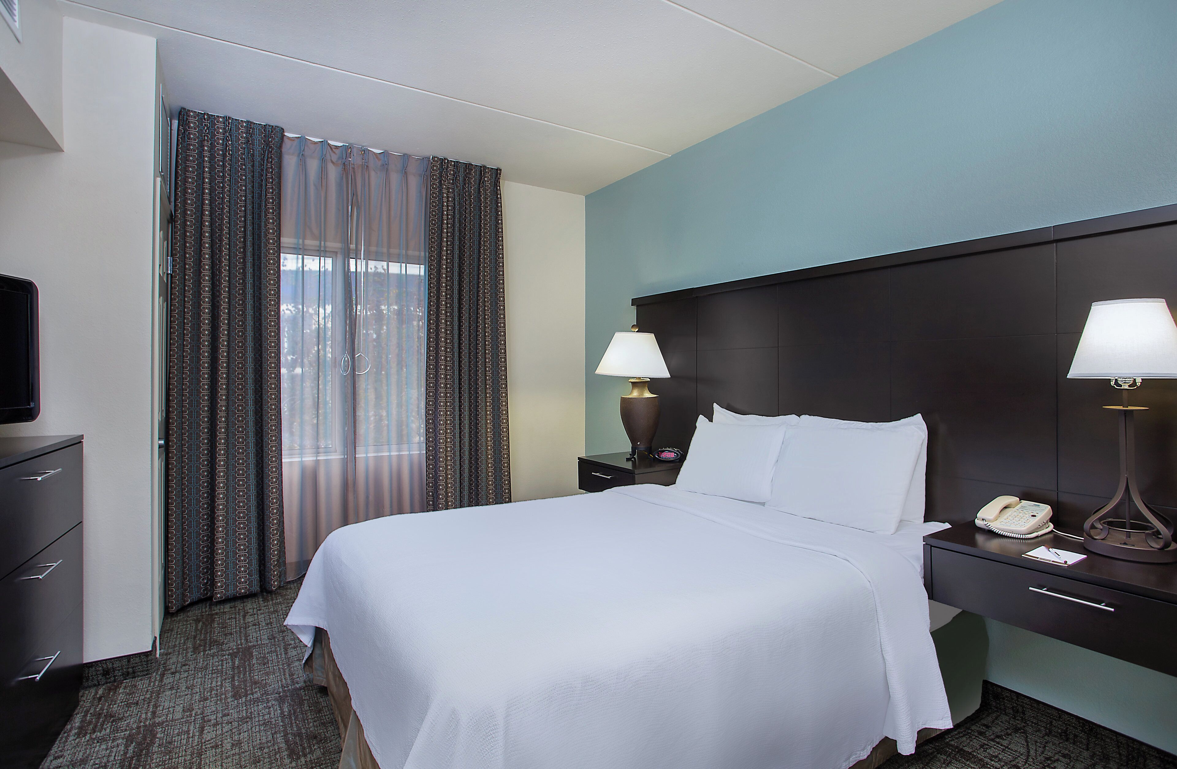 A hotel room with a bed, a TV, a desk with a lamp, and a telephone.