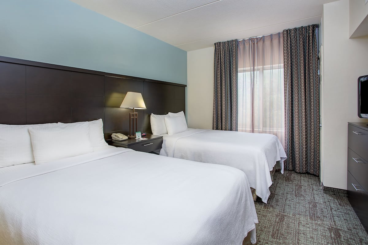 Habitación de hotel con dos camas, una mesita de noche con lámpara, televisión y ventana con cortinas.