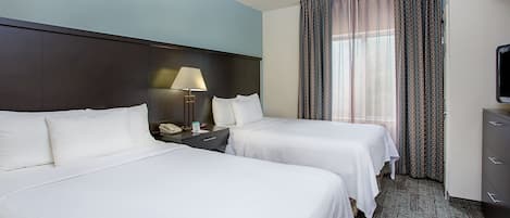A hotel room with two beds, a nightstand with a lamp, a TV, and a window with curtains.