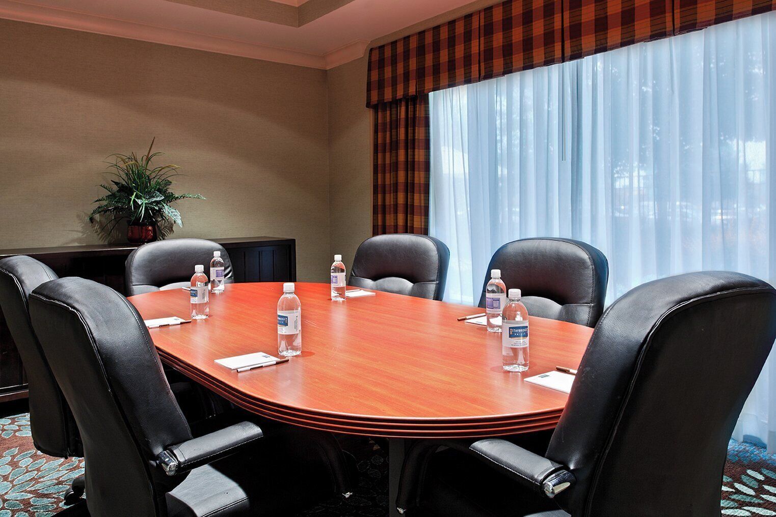 Une salle de conférence avec une table ronde, six chaises, des bouteilles d’eau et une plante en pot.
