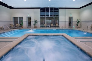 A hotel pool area with a hot tub, lounge chairs, and a seating area with tables.