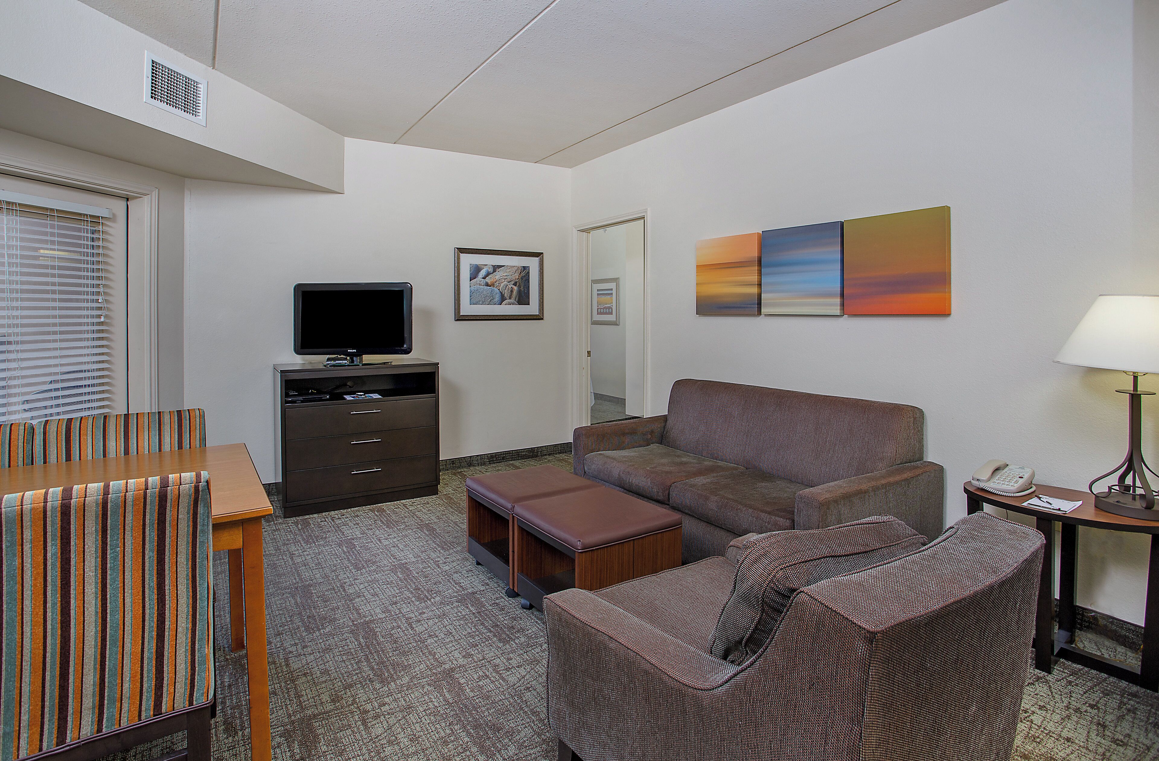 Habitación de hotel con sofá, una mesita, televisor y una obra de arte en la pared.