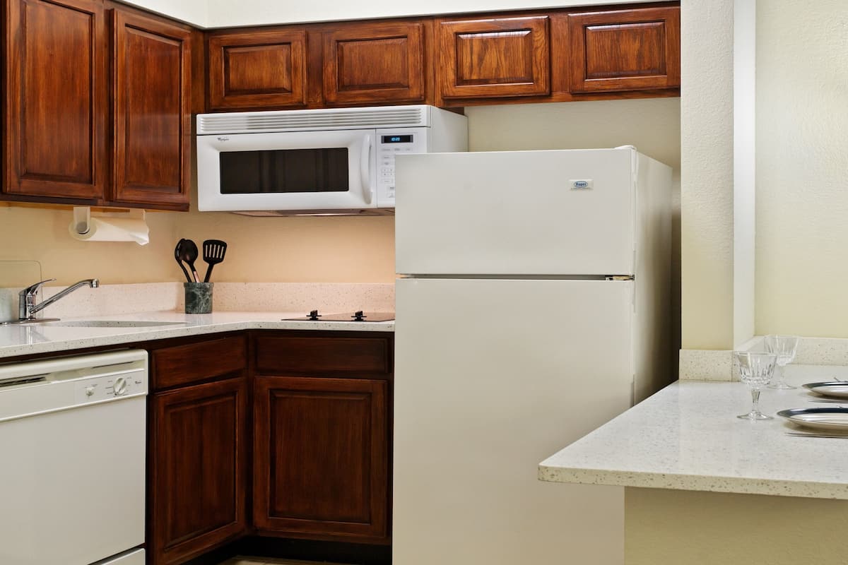 Cocina compacta con armarios de madera, un refrigerador blanco, un microondas y un pequeño comedor con mesa y sillas.