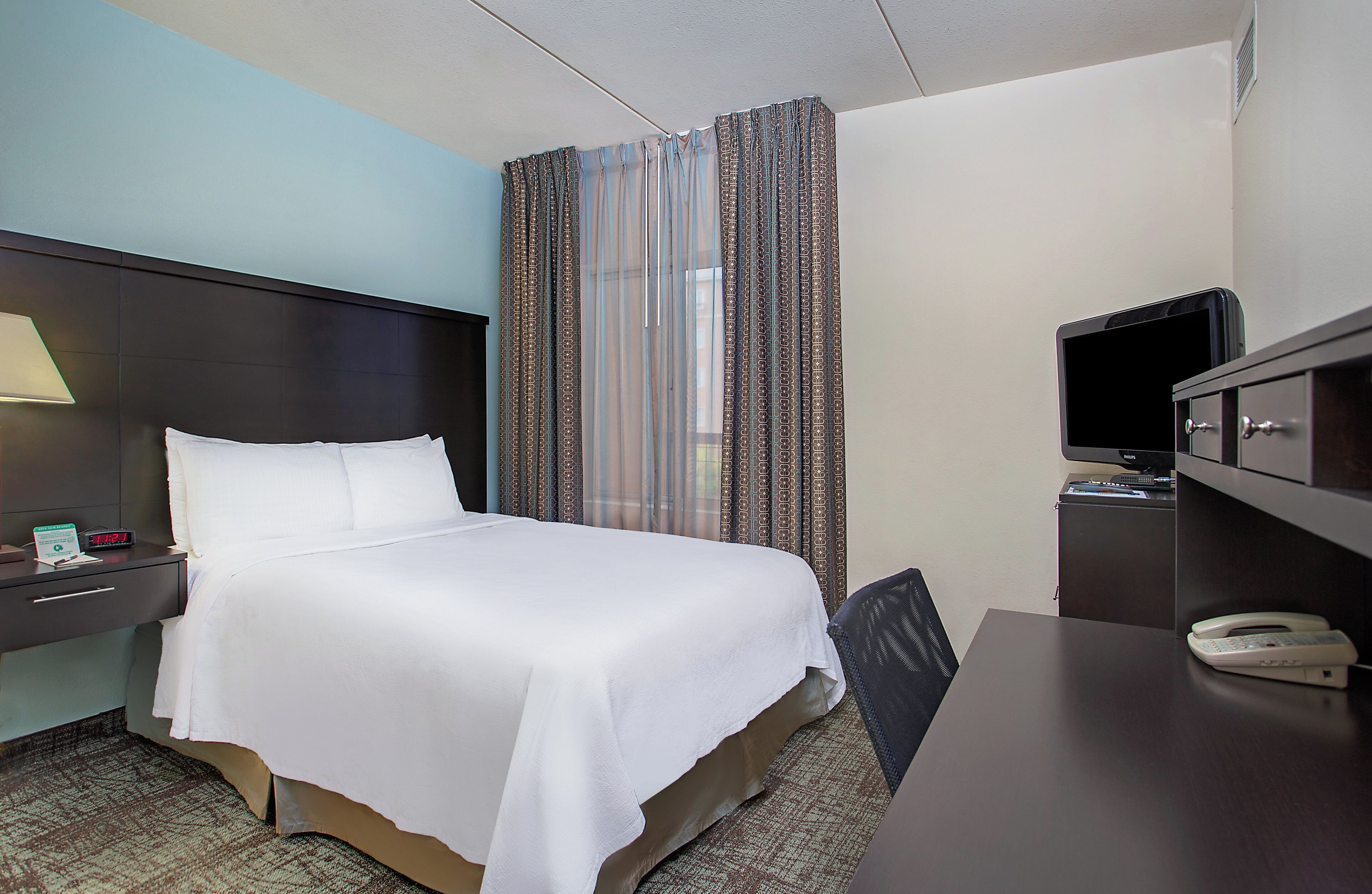 A hotel room with a bed, a desk, a television, and a telephone.