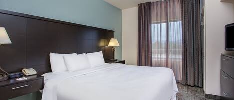A hotel room with a large bed, two bedside tables with lamps, a TV, and a window with curtains.