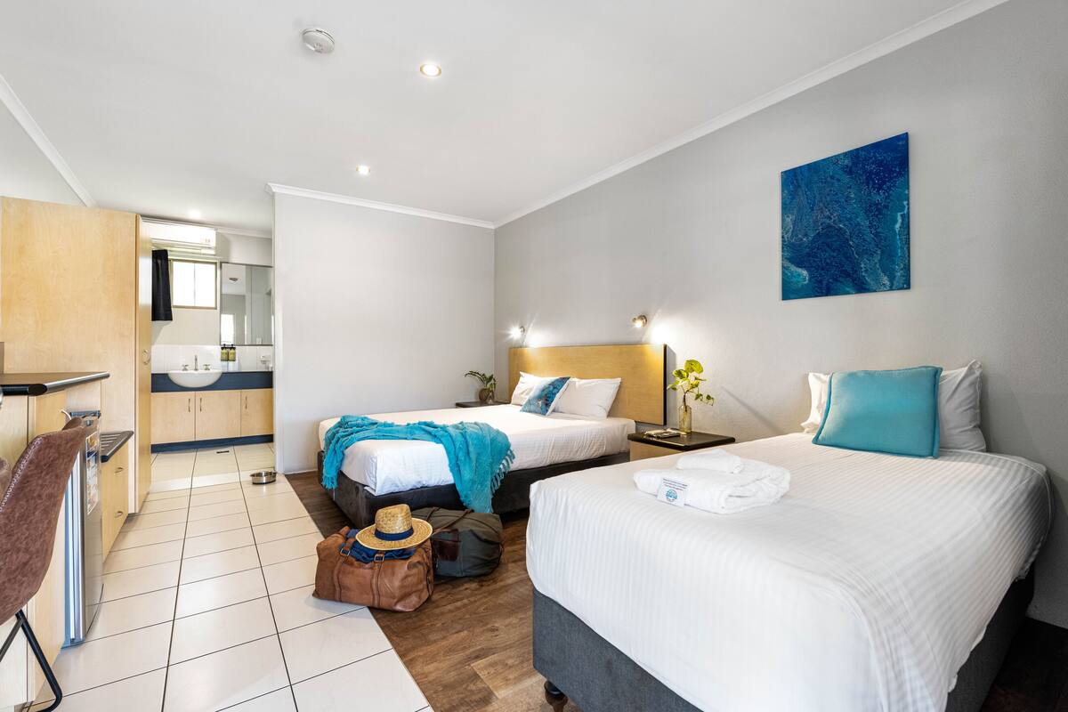 A hotel room with two beds, a kitchenette, a bathroom, and a large window.