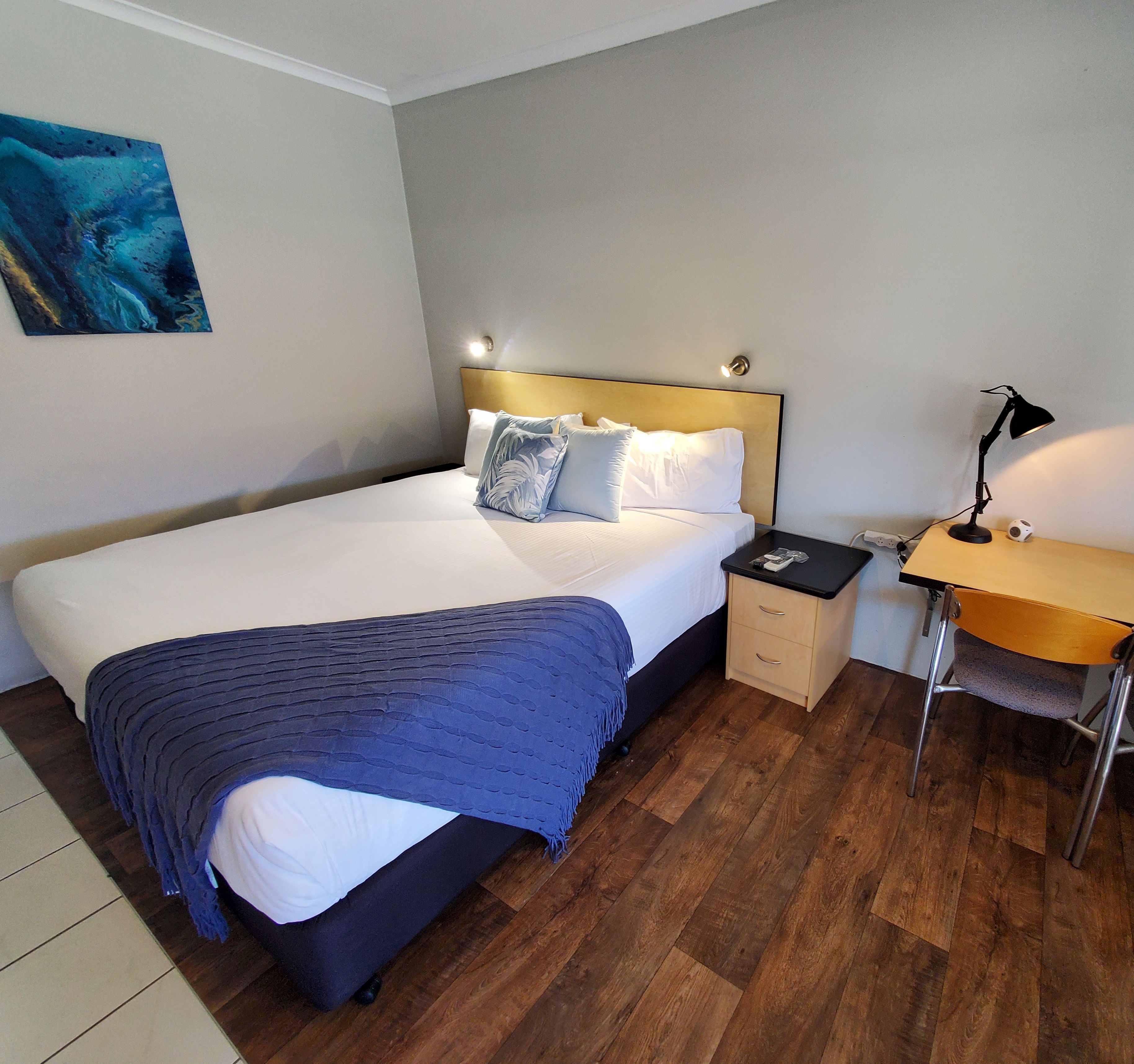 Habitación de hotel impecable con una cama grande, una mesita de noche, un escritorio con silla y una lámpara de pared.