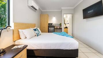 Habitación de hotel con cama, mesita de noche, lámpara, aire acondicionado, televisor y vista al área de la cocina.