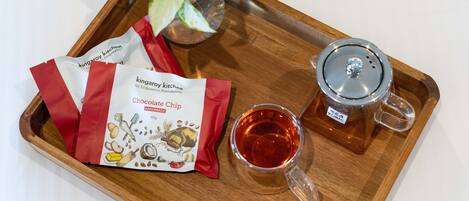 Una bandeja con dos paquetes de galletas con chispas de chocolate, una taza de vidrio con té y una pequeña planta en maceta.
