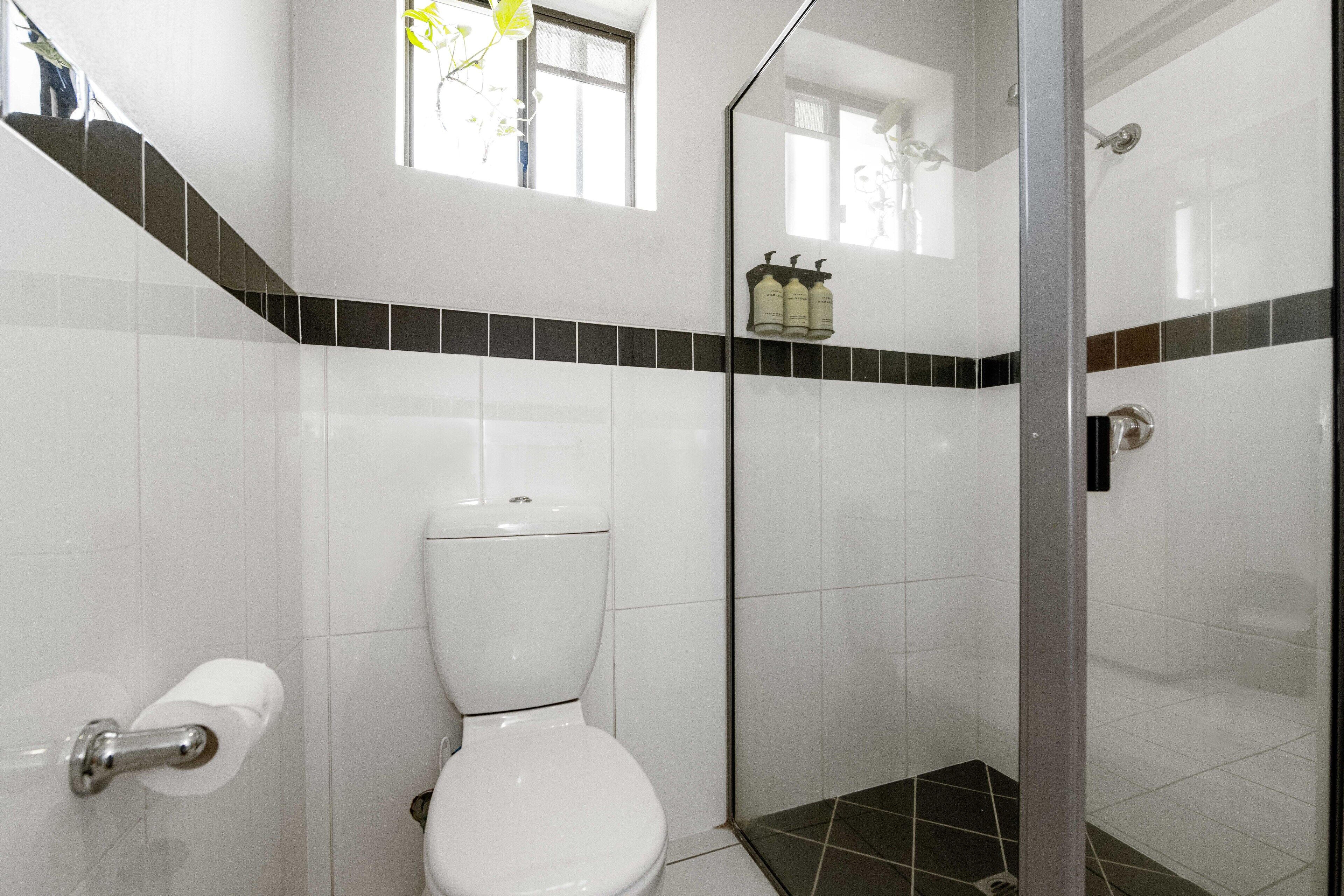 A bathroom with a toilet, a shower, and a window.