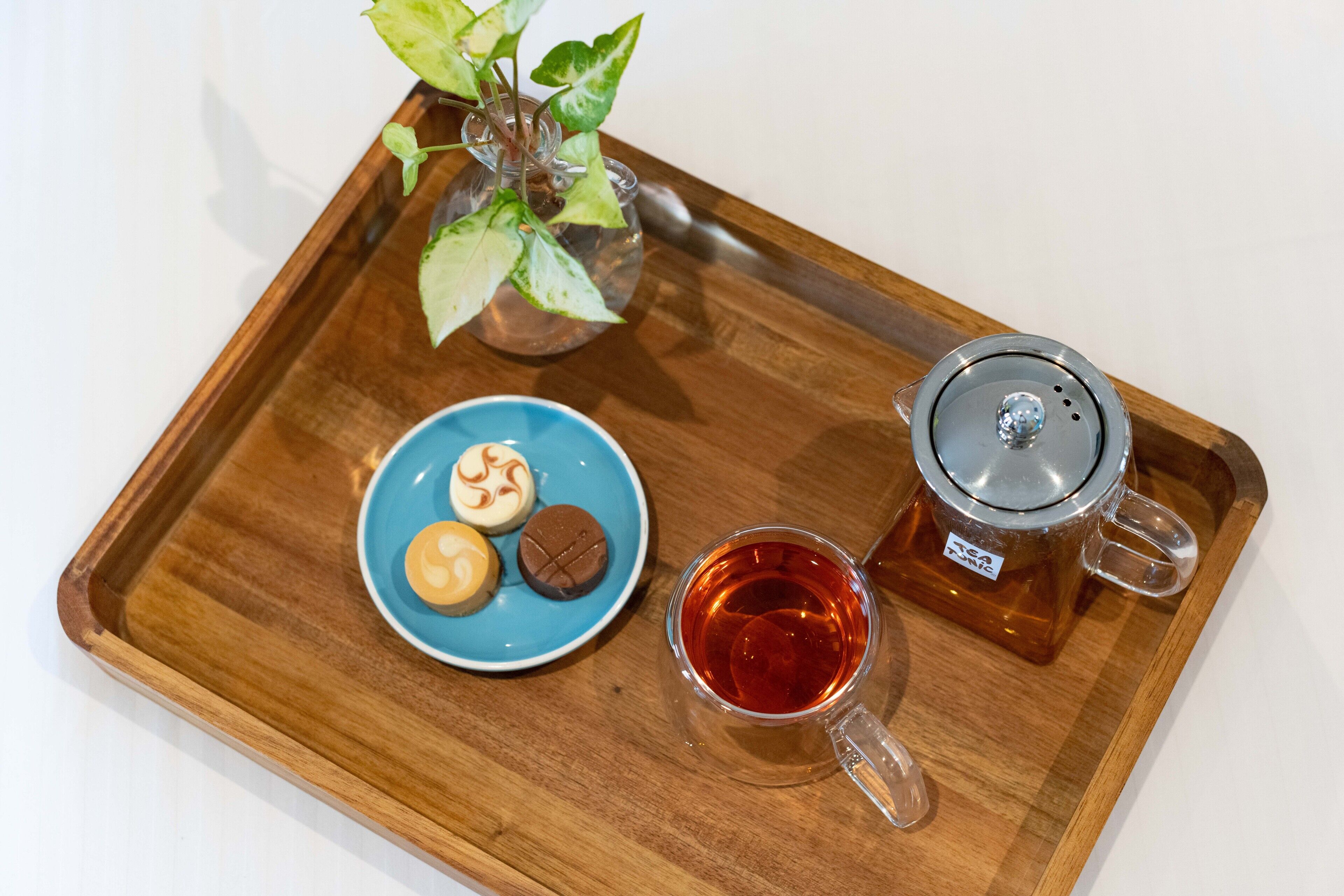 A wooden tray with a teapot, a cup of tea, and a plate with cookies.