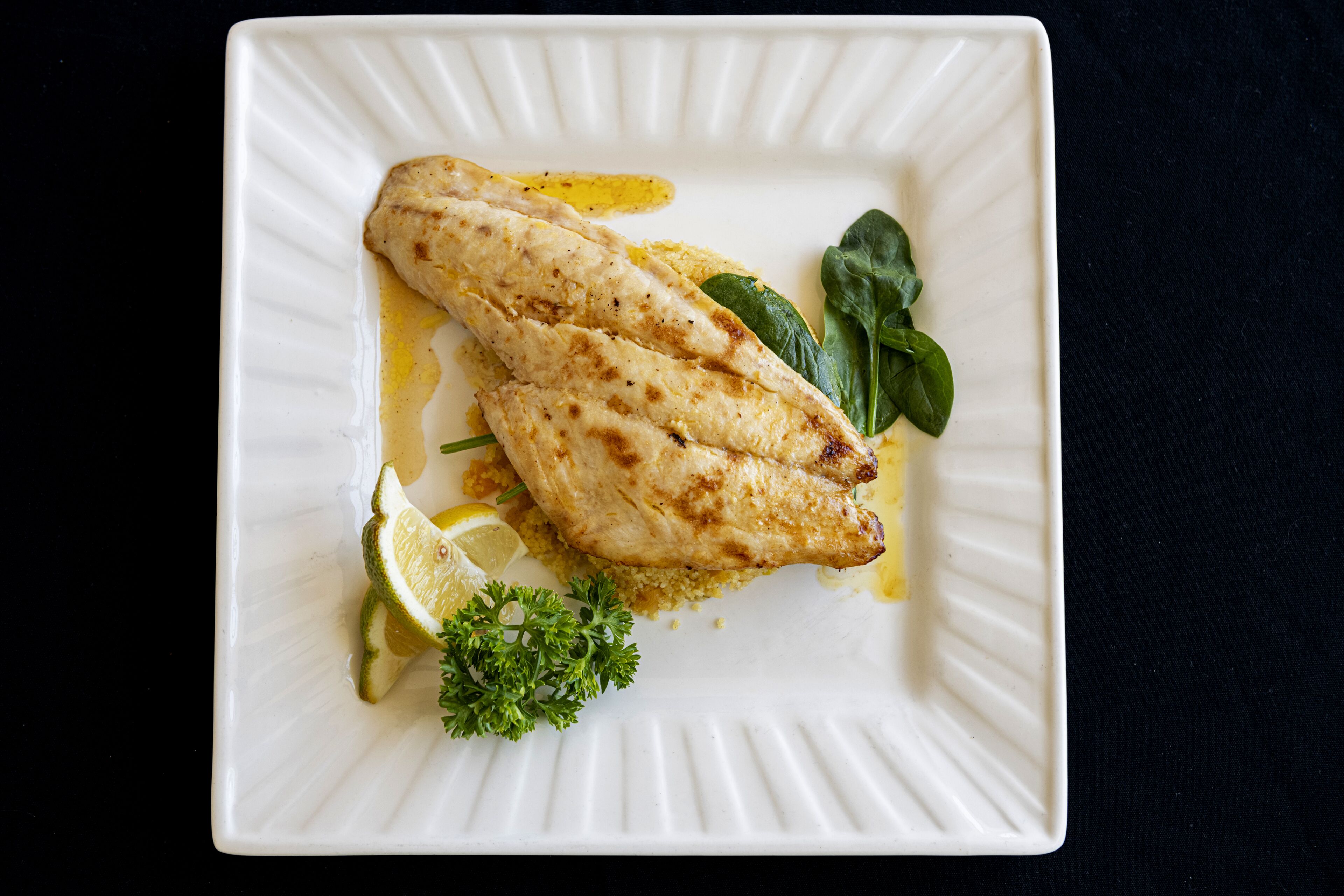 A white plate with grilled fish, lemon slices, and parsley.