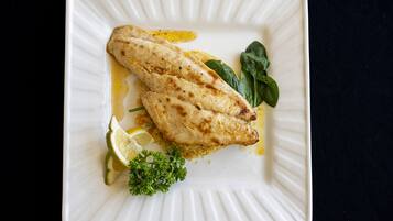 A white plate with grilled fish, lemon slices, and parsley.