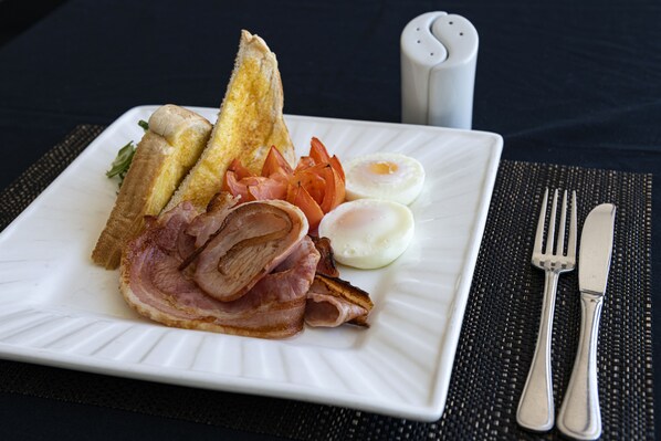 A plate with toast, eggs, bacon, and tomatoes on a white plate. - Alara Motor Inn (West Mackay)