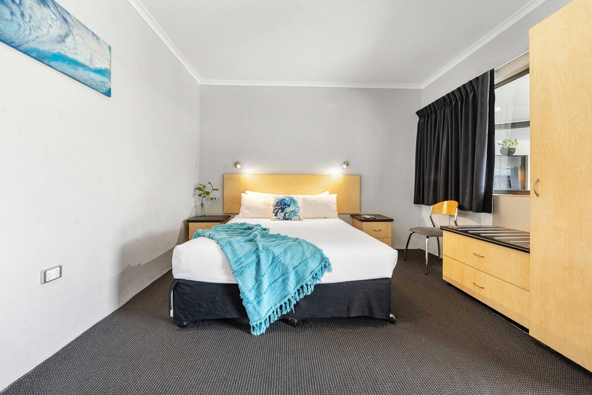 A hotel room with a bed, a nightstand, a dresser, a mirror, and a painting on the wall.