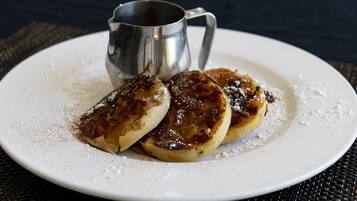 A plate with two pancakes and a metal cup on a dark surface.
