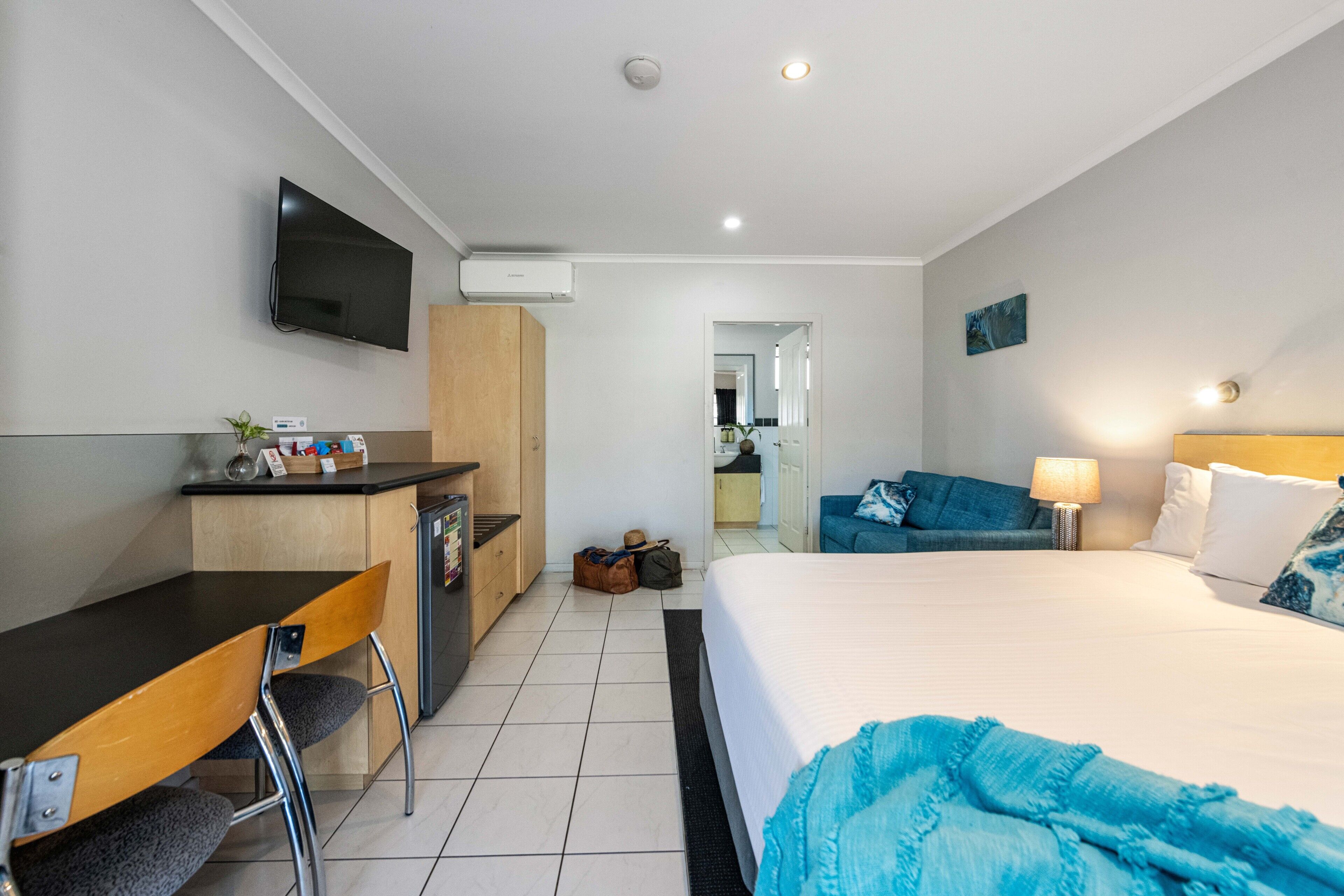 Quarto de hotel com cama, escrivaninha, cadeira, televisão e banheiro visível por uma porta aberta.