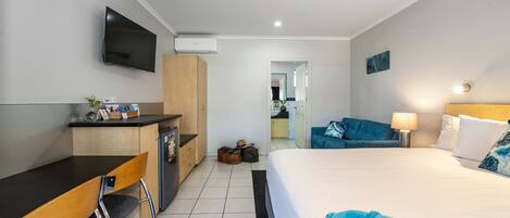 Quarto de hotel com cama, escrivaninha, cadeira, televisão e banheiro visível por uma porta aberta.