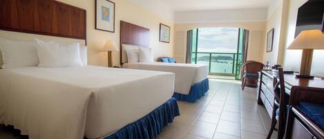 A hotel room with two beds, a desk, and a view of the sea.