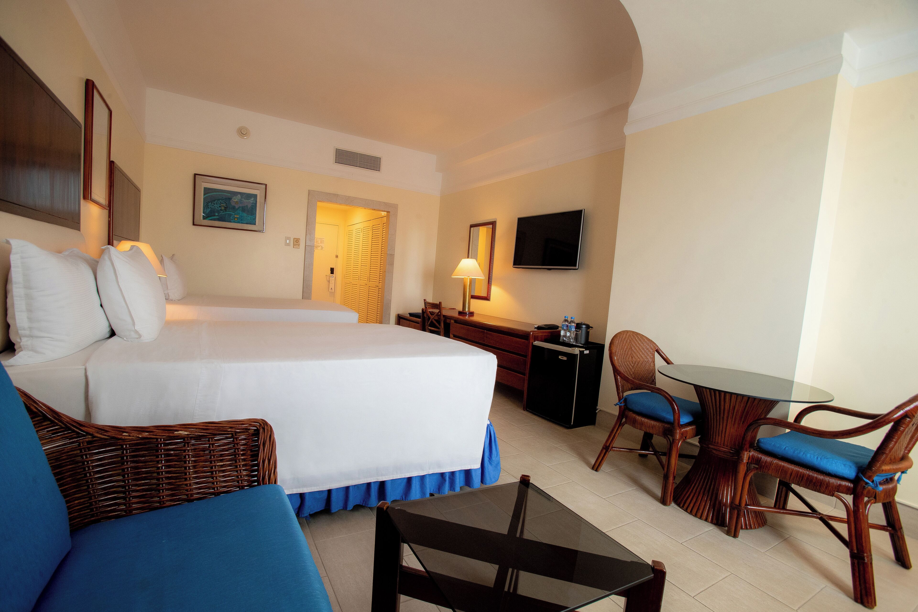 A hotel room with a large bed, a desk, a chair, a small table, and a TV.