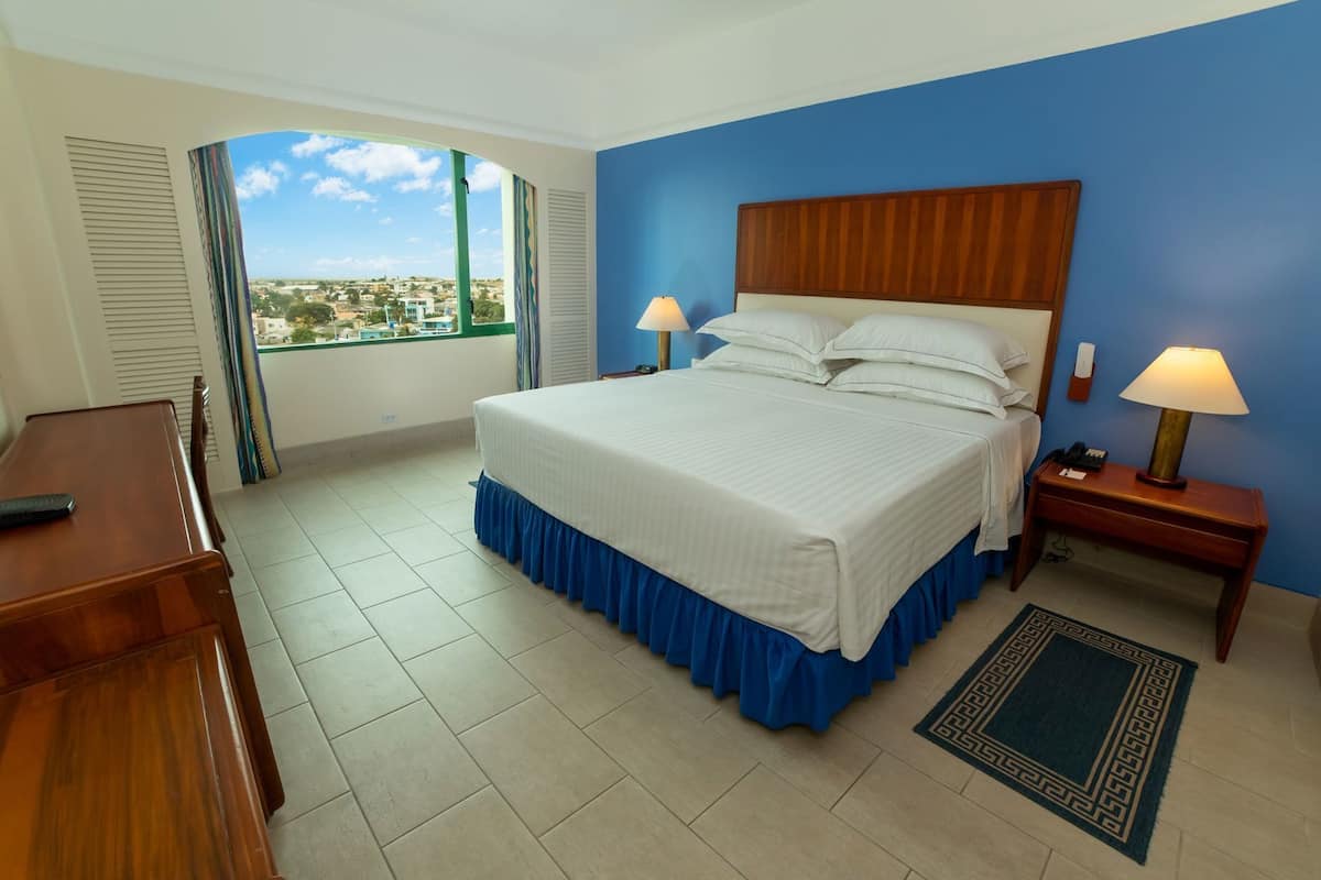 A hotel room with a bed, bedside lamps, a desk, and a view of the city.