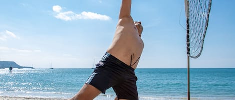 A beach volleyball player in mid-air, reaching for a volleyball near a net.