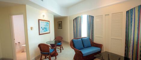 A living room with a wicker sofa, a glass coffee table, and a dining area with chairs and a table.