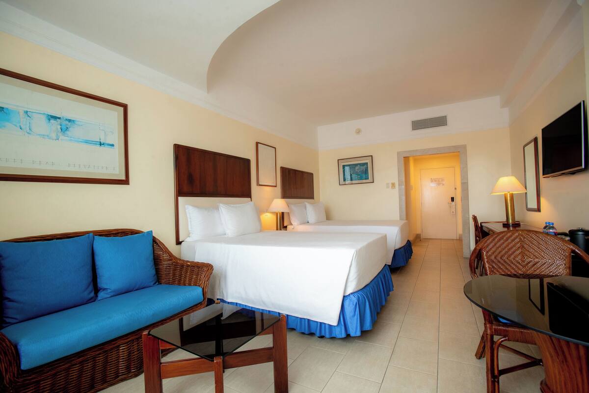 A hotel room with a bed, a sofa, a dining table, and a TV.